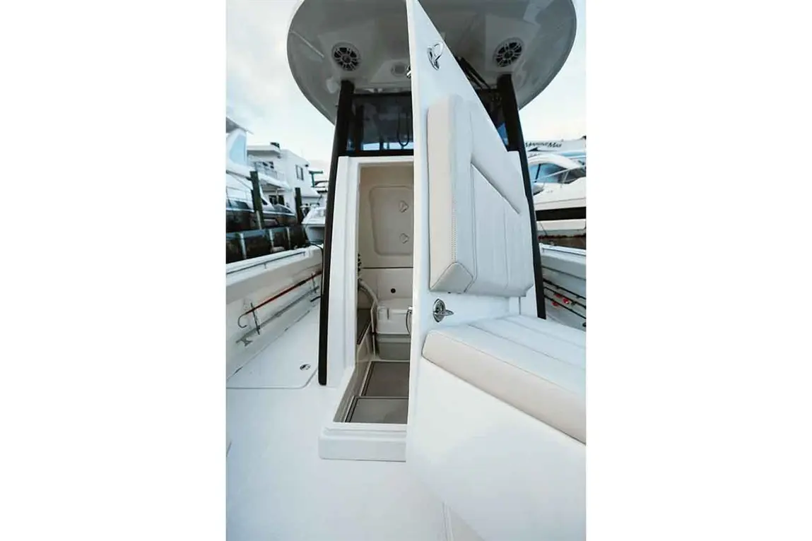 A white boat features an open compartment door, showcasing a clean interior and cushioned seating with a waterfront view.